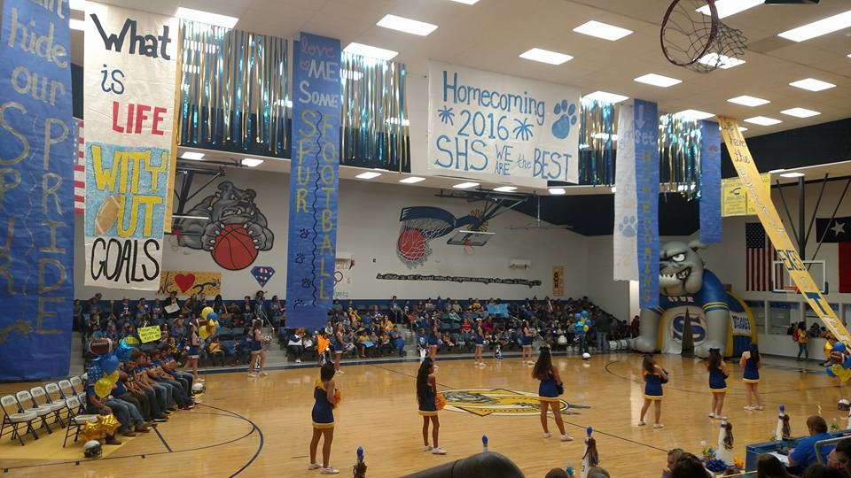 People gathered all together in the gym, a group of cheerleaders dancing and cheering on the basketball team.