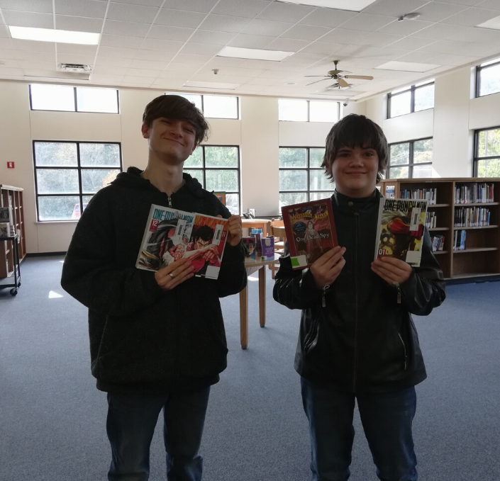 Two teenagers holding up volumes of famous known manga such as "One Punch Man" and "One Piece"