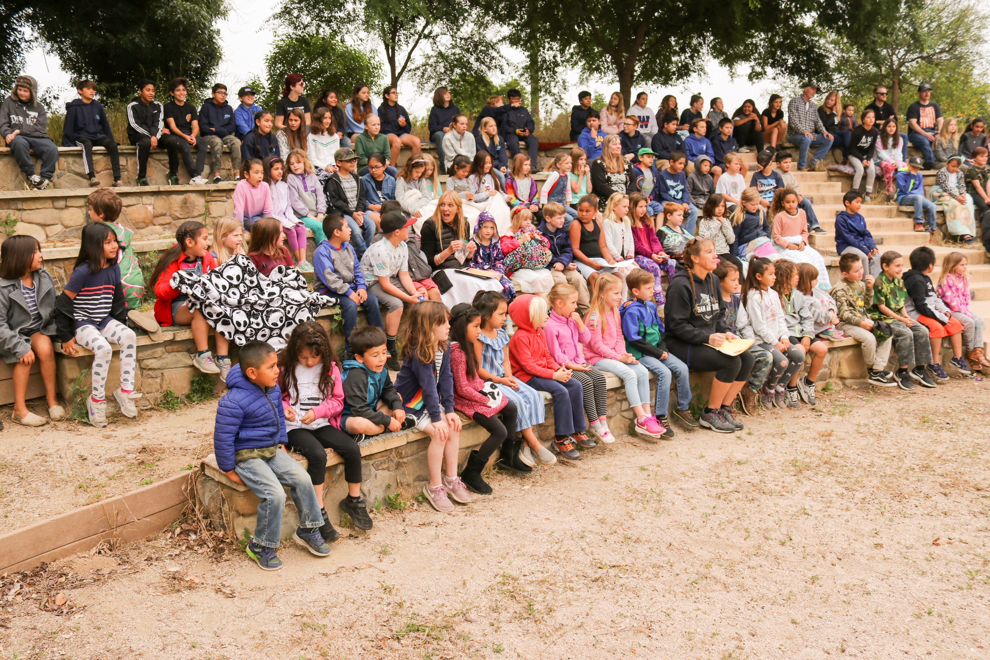 The kids all sitting outside in the school's bleachers made out of wood