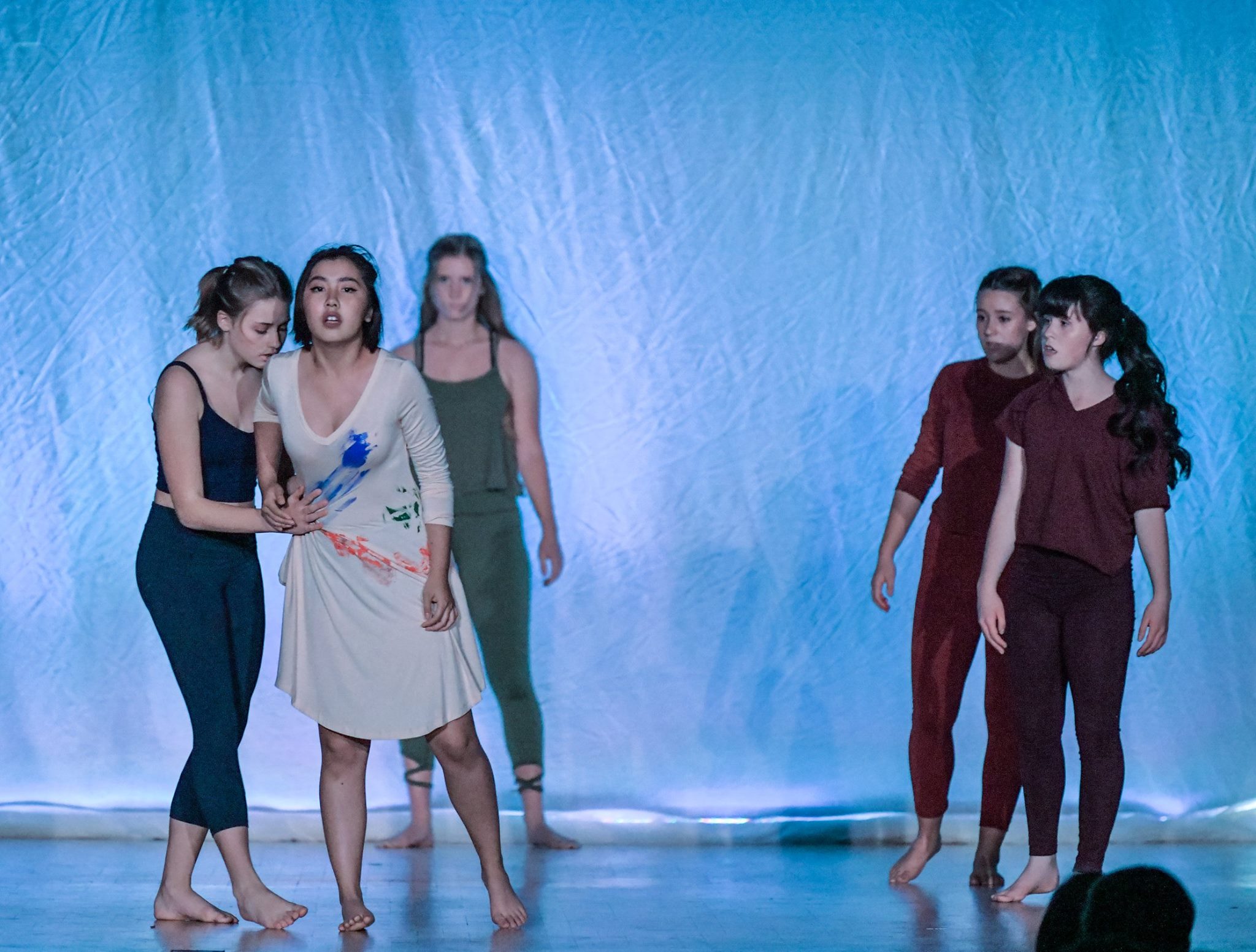 Five girls on the stage, one holding to the other and the other three looking right back at them