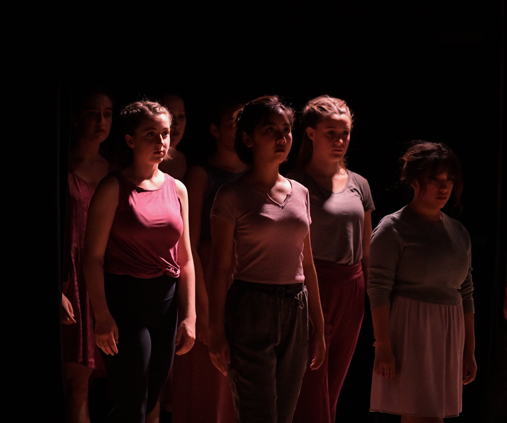 Seven girls standing still, the lighting shinning above their heads
