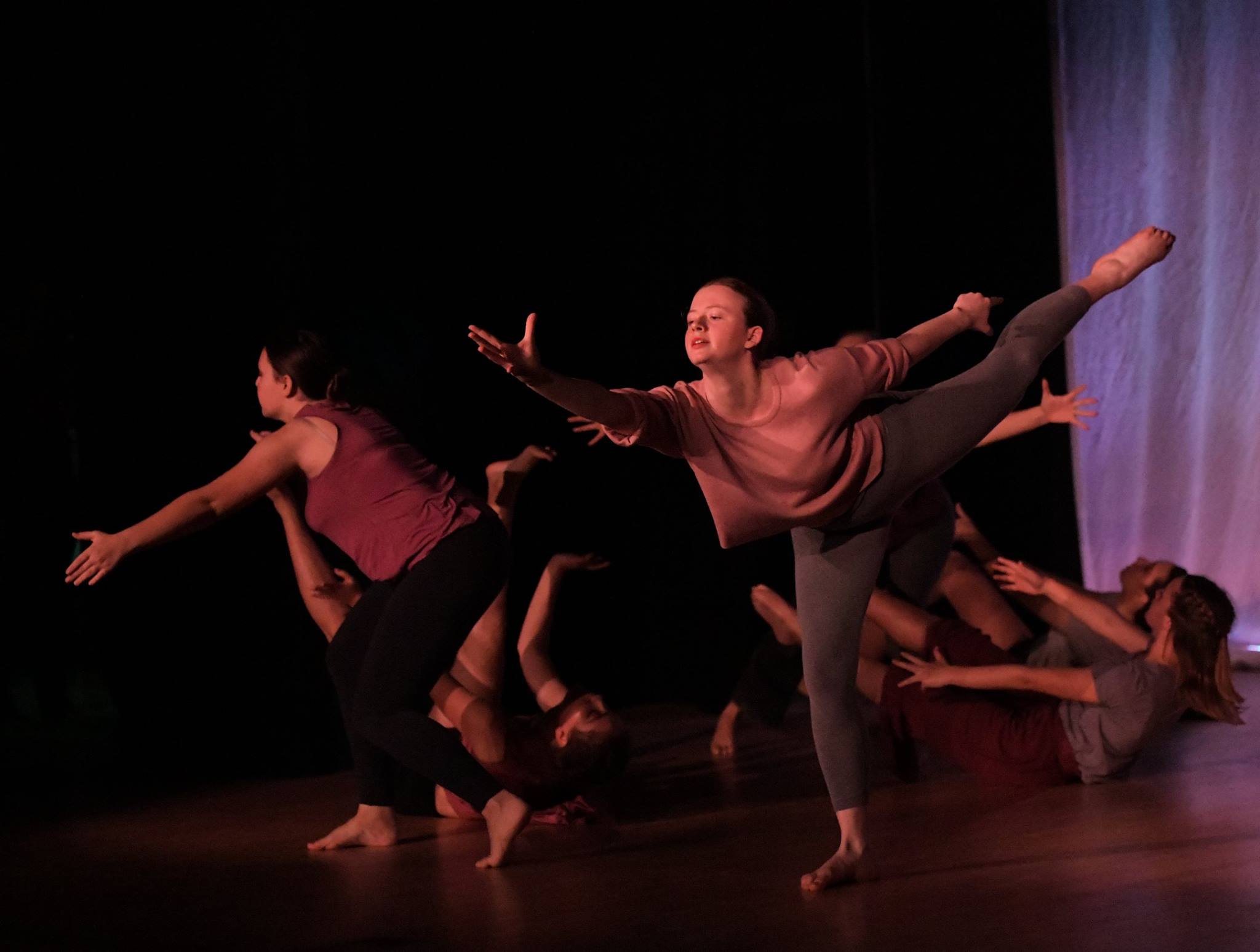 A photo of the performance, a group of the girls dancing at the floor and the others stretching and lifting up one of their legs