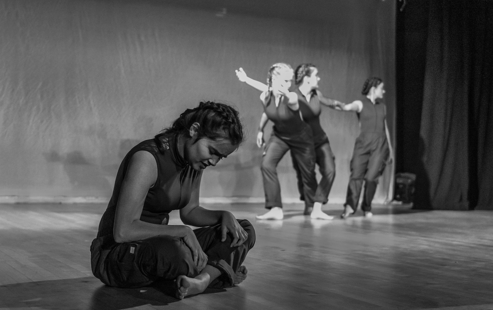 A monochromatic photo, the girl closest to the camera sitting and the other three performing at the back of the stage