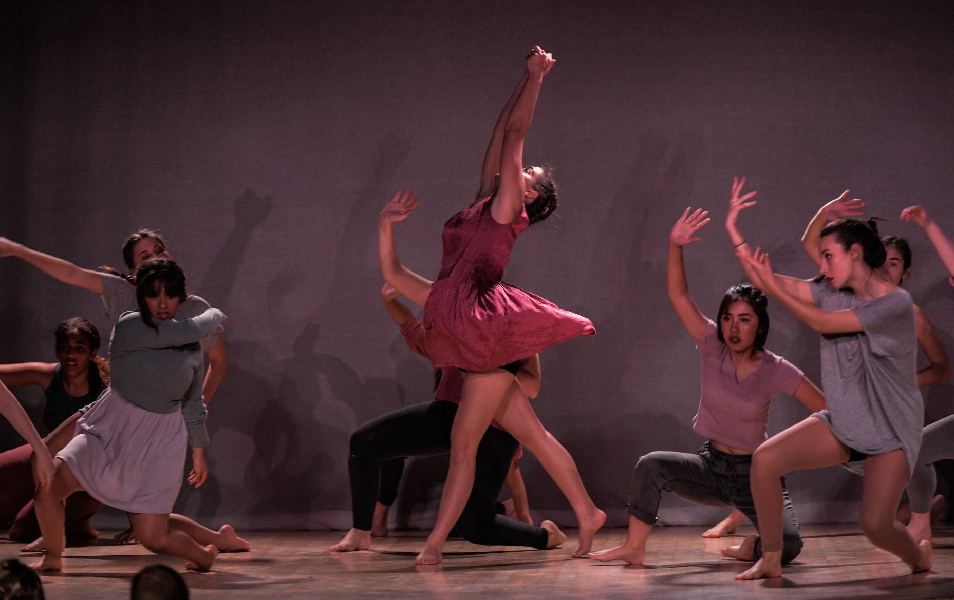 A girl standing in the middle of the group, holding her hands up to the sky while the other still dance around her