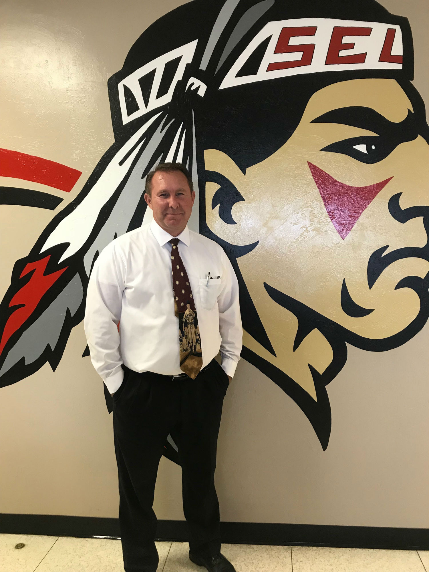 A photo of Principal Dennis Thompson in front of a school mascot mural