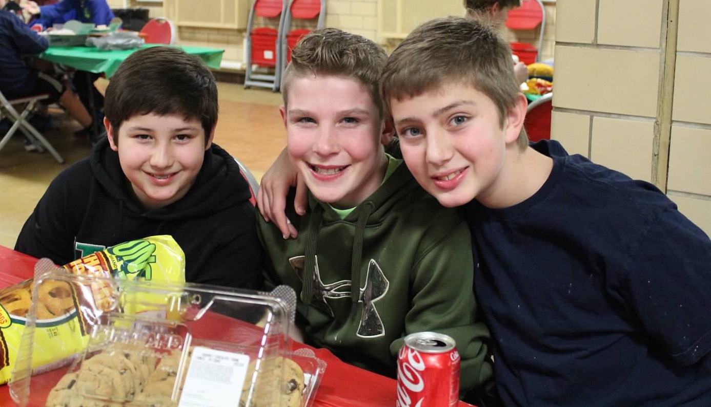 Three 7th graders sitting at a lunch table smiling at the camera