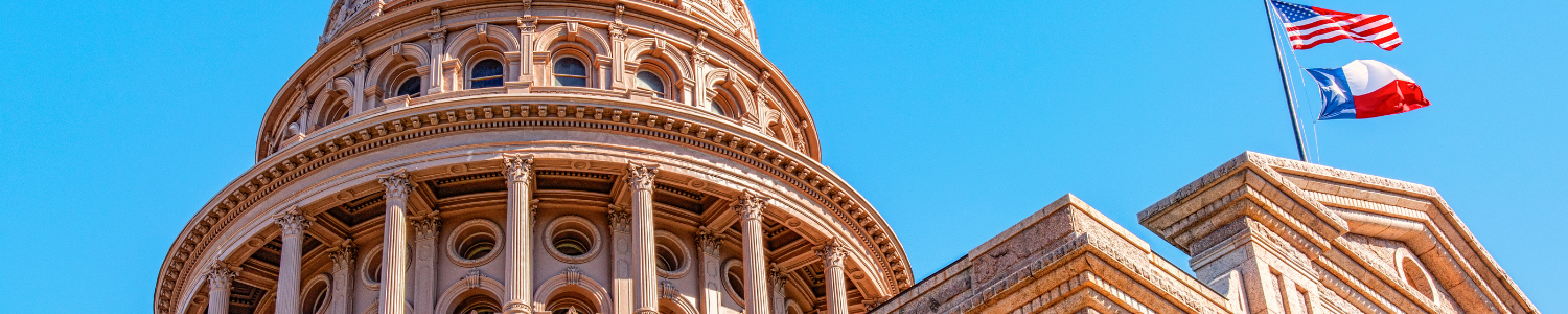 Texas State Capitol dome with American & Texas flags flying, blue sky background