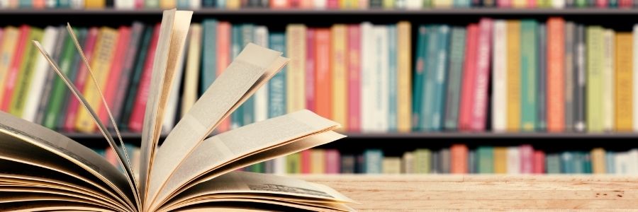 Picture of wall of colorful books with an open book sitting on a desk