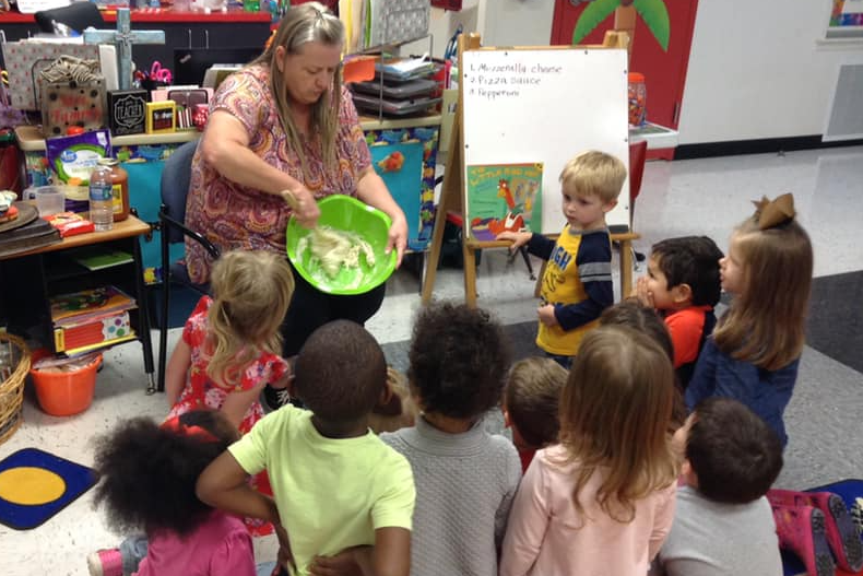 Teacher demonstrates how to mix pizza dough while students help